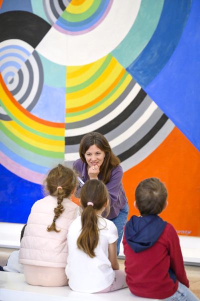 Petite groupe d'une philosophe et trois enfants qui discutent devant œuvre colorée de Robert Delaunay